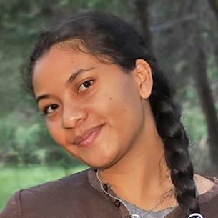 Portrait of a smiling young woman with a dark braid, outdoors in a green park setting.